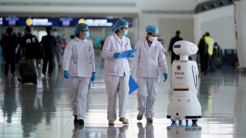 Medical workers walk by a police robot in Wuhan, China