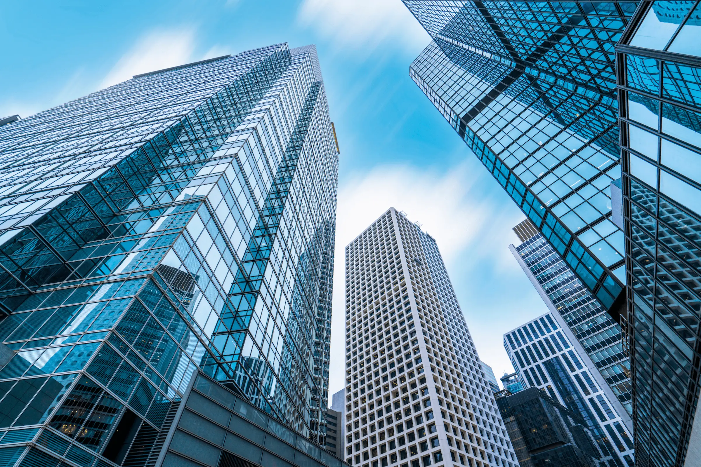 A perspective view of modern high-rise office buildings with reflective glass windows under a clear blue sky, representing enterprise software development and technological innovation.