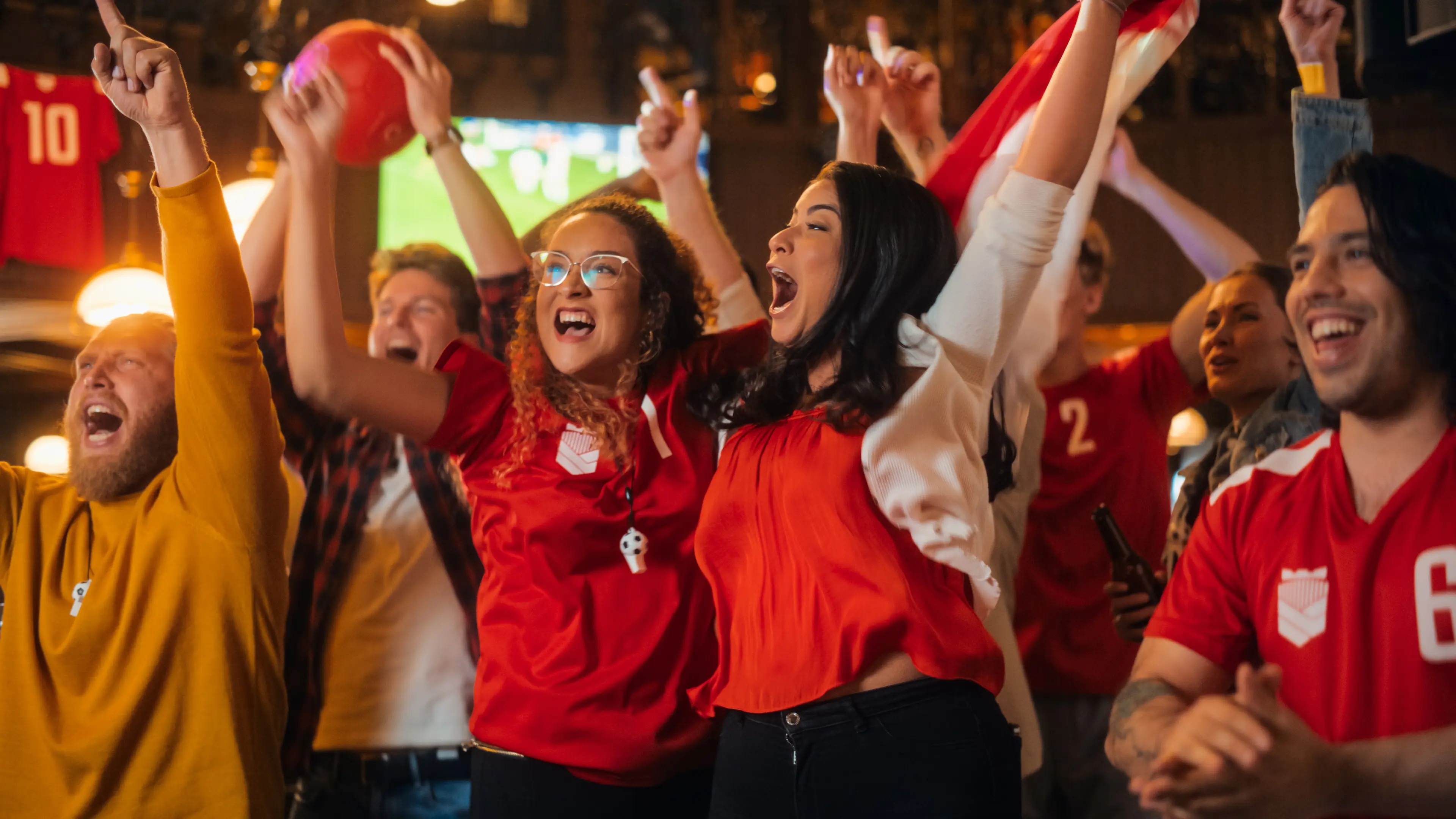 A group of diverse sports fans cheering and celebrating in a bar, representing the success of a unified fan experience platform.