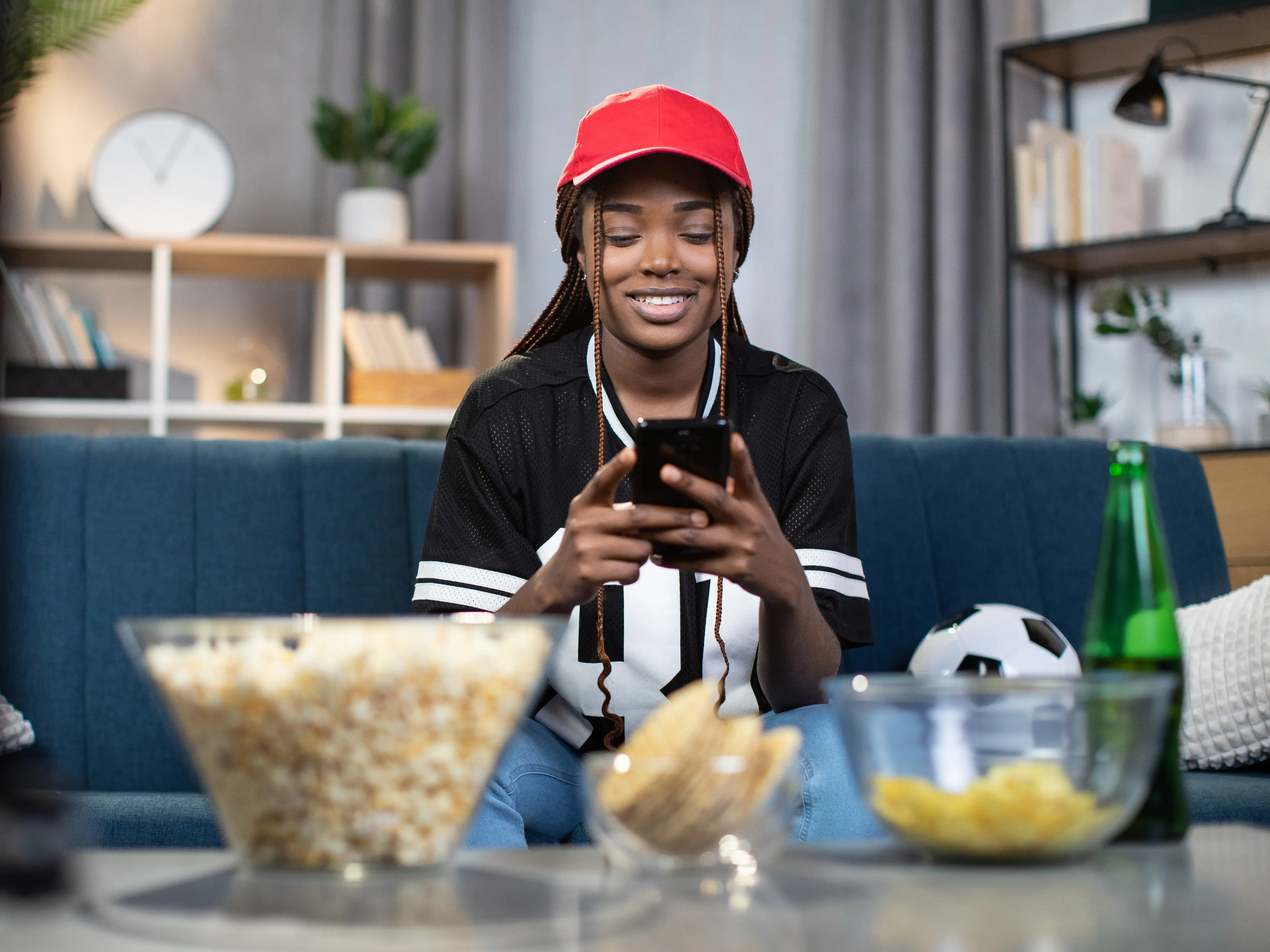 A smiling sports fan using a mobile application on her smartphone while watching a game at home, representing high fan engagement and digital platform success.